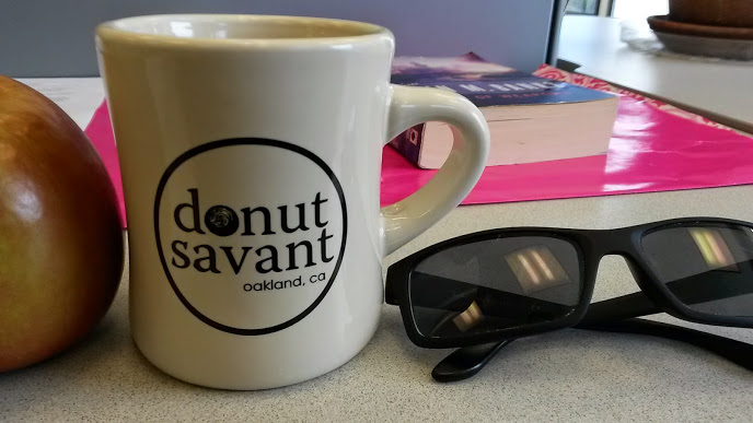 a photo of an apple, a mug reading Donut Savant, and some sunglasses